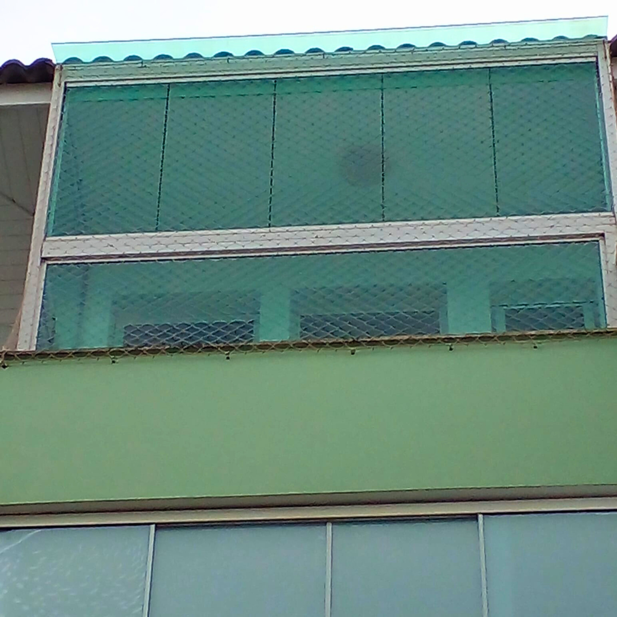 Fachada de prédio com varanda ou área de serviço protegida por rede de segurança instalada em toda a abertura.