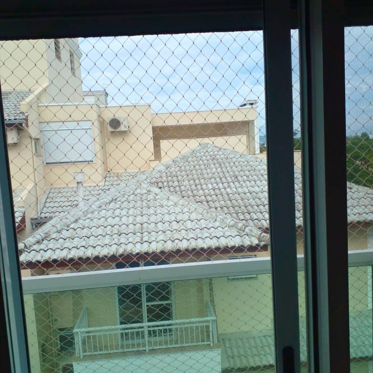 Porta de vidro de correr com rede instalada, focando na segurança sem bloquear a vista dos telhados vizinhos.