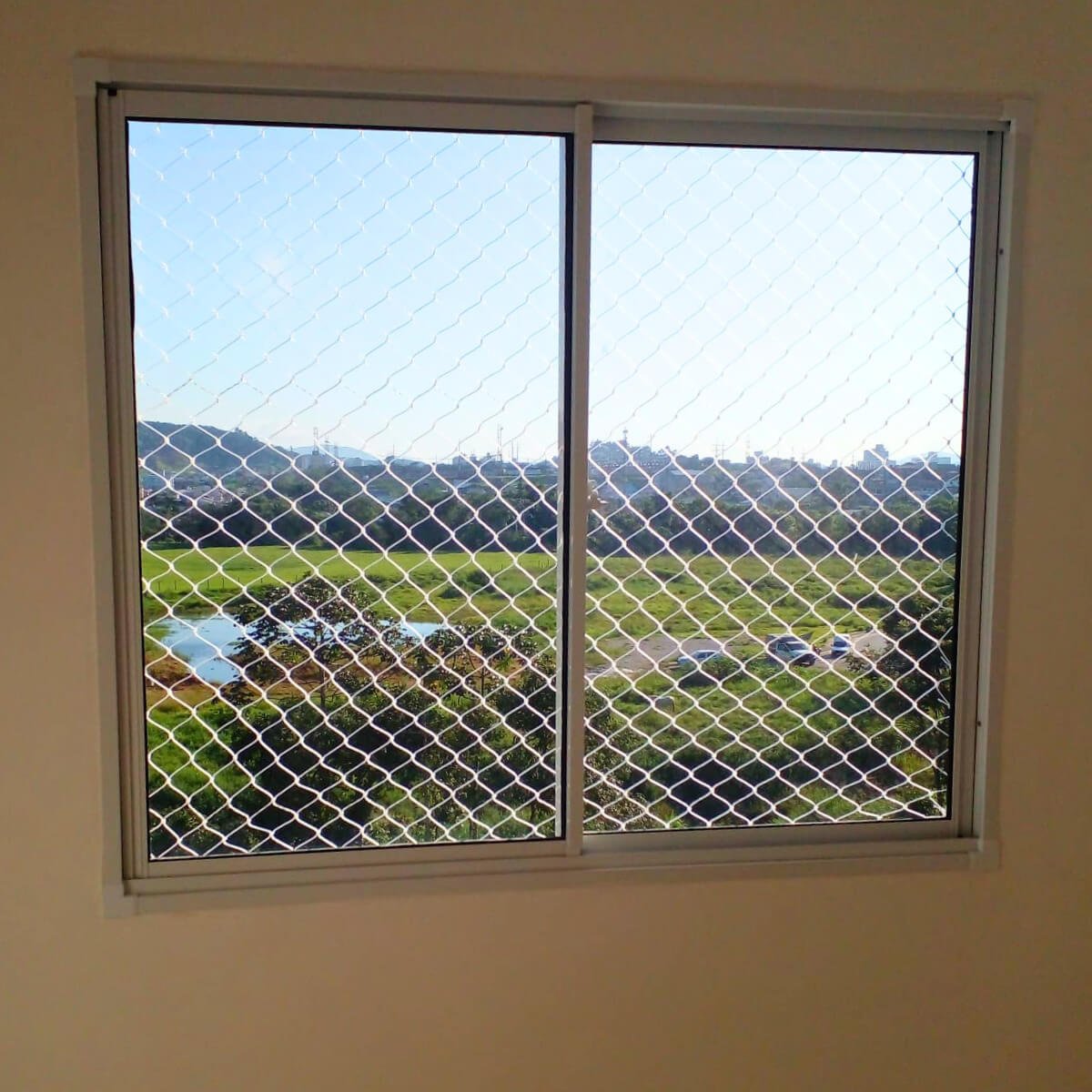 Rede de segurança em janela de apartamento com vista para área de preservação ambiental.