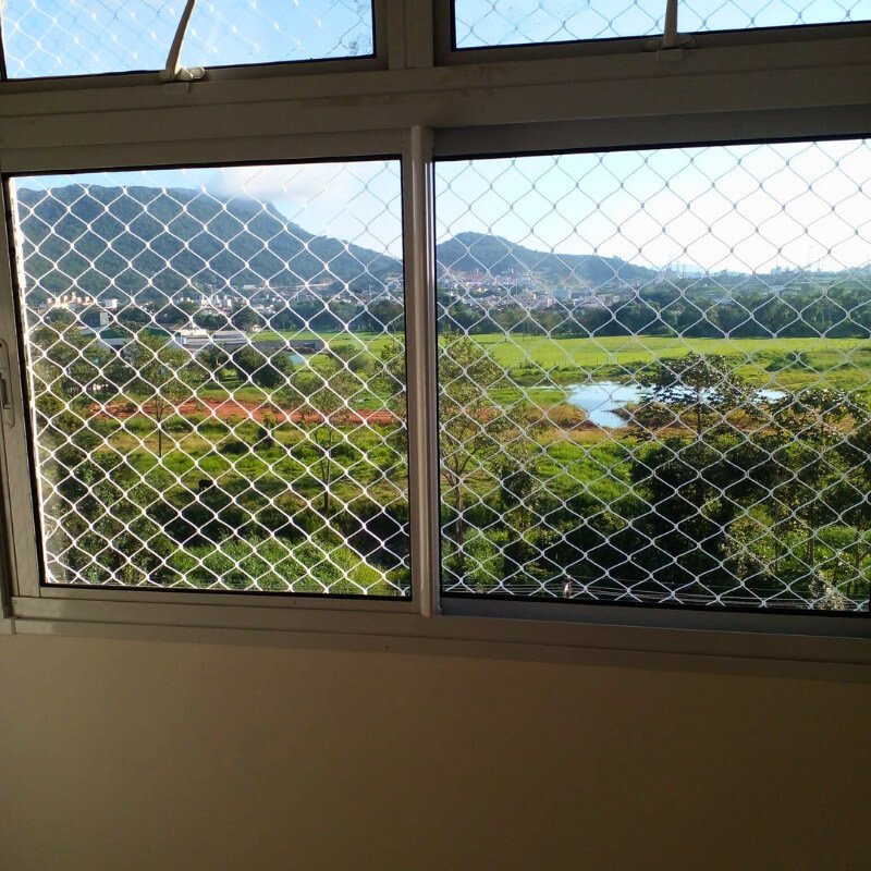 Janela ampla com rede de segurança instalada e vista para natureza e montanhas.