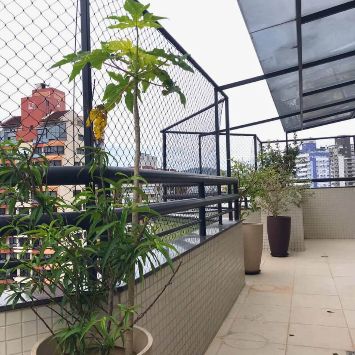 Terraço amplo com plantas e fechamento perimetral em rede de proteção com estrutura metálica preta.
