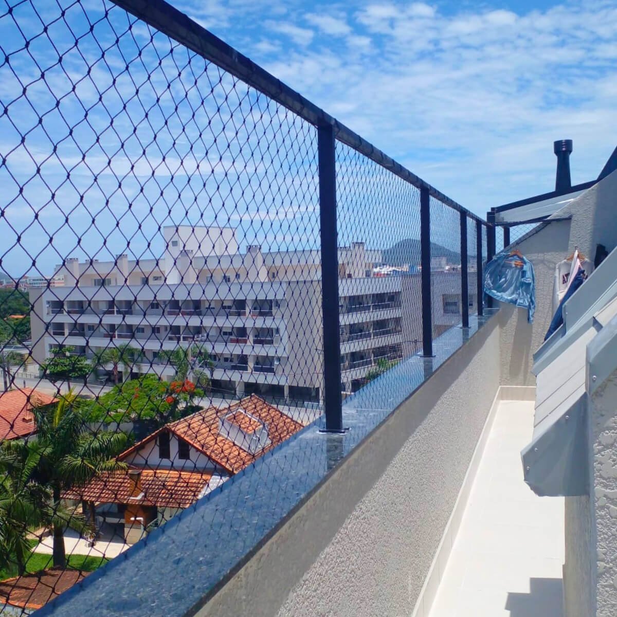 Varanda estreita com rede de proteção fixada em hastes metálicas pretas sobre a mureta.
