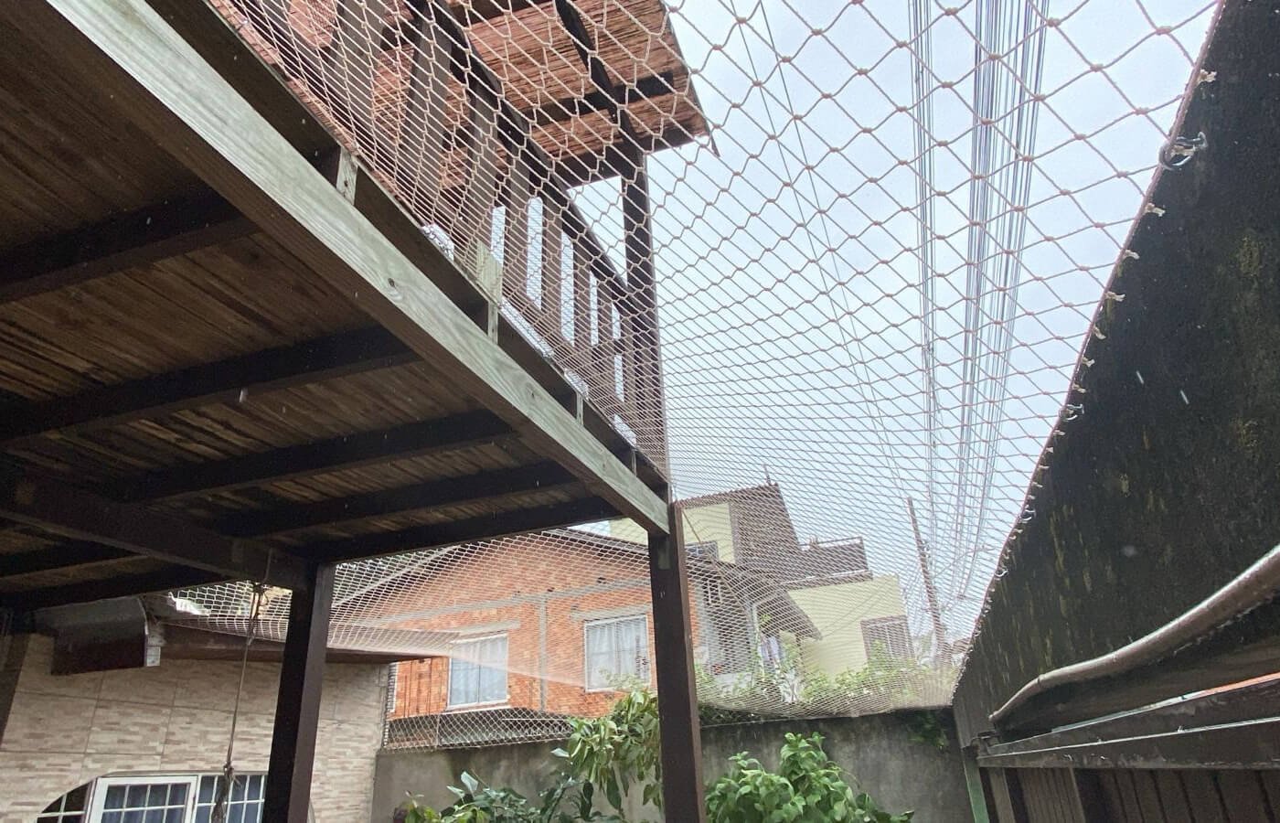 Estrutura de madeira (pergolado) totalmente cercada por rede de proteção, formando um gatil ou área segura.