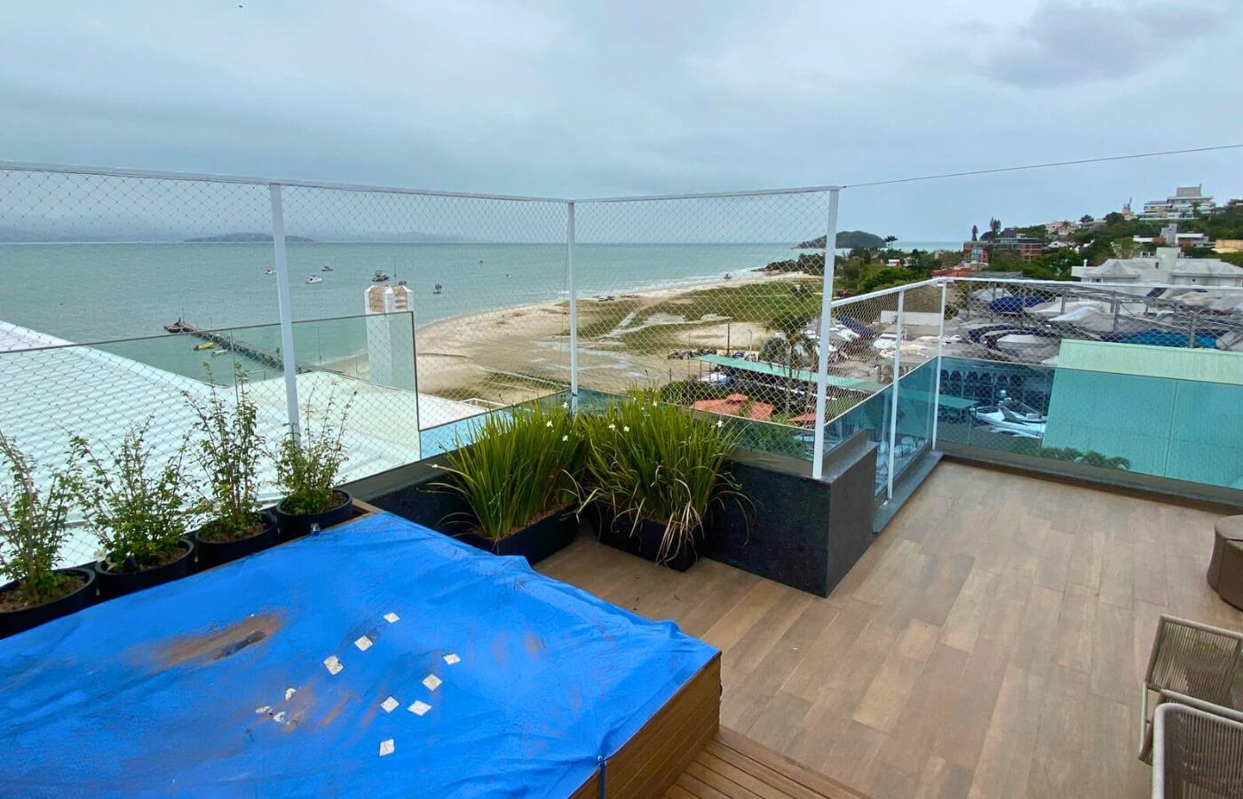 Canto de área de lazer em cobertura com vista para o mar, protegido por guarda-corpo de vidro e extensão em rede.