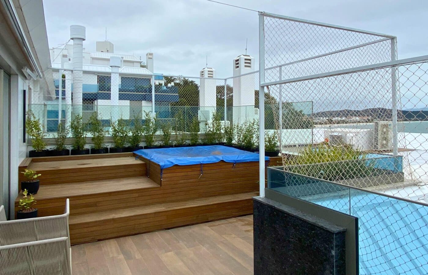 Deck de madeira com degraus e jacuzzi coberta em terraço, cercado por estrutura de segurança com rede branca.