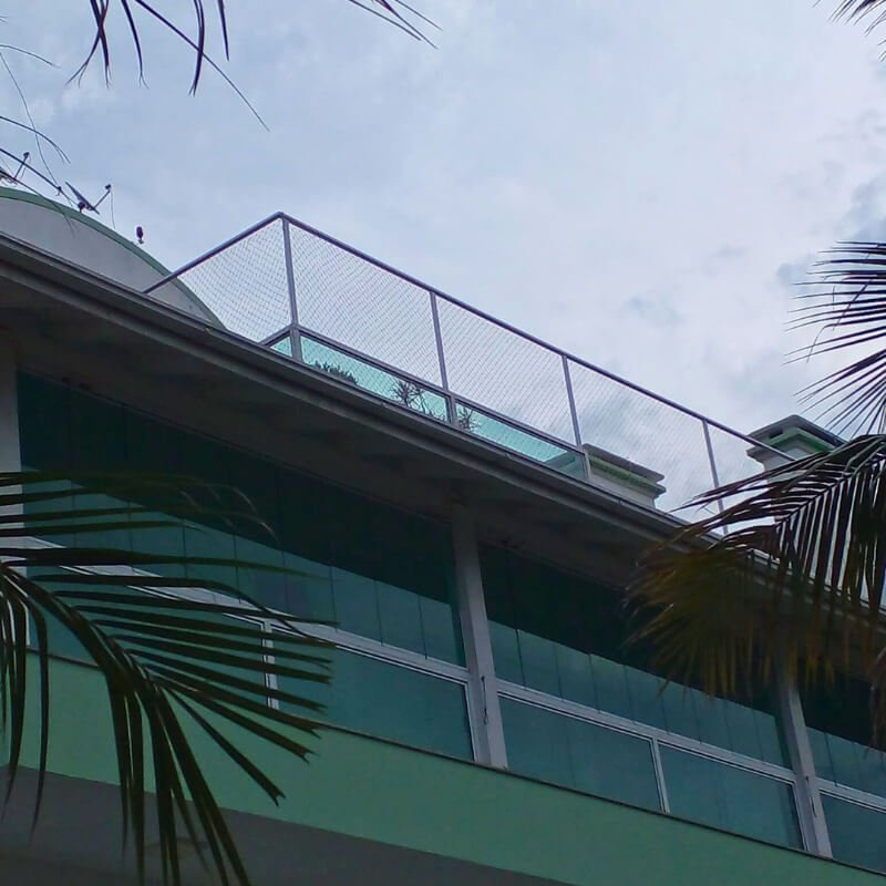 Fachada de prédio com vidros verdes e sacada no último andar protegida por rede de segurança instalada no guarda-corpo.