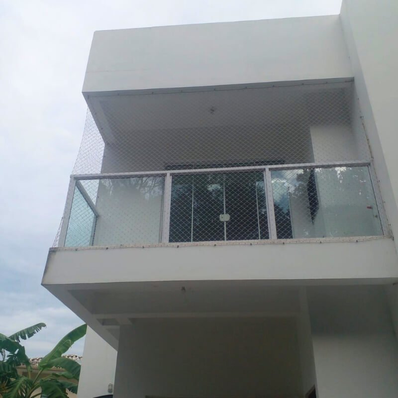 Fachada de residência moderna branca com sacada de vidro fechada por rede de proteção discreta.